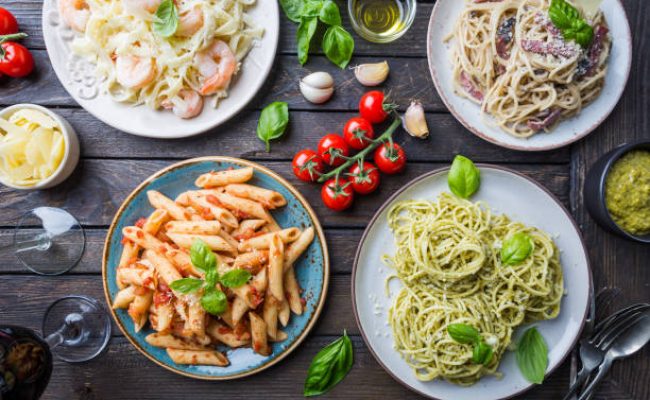 Several plates of pasta with different kinds of sauce over wooden background, top view. Concepts of Italian food.